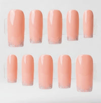 Ten square press-on nails arranged in two rows on a clear display stand against a white background. The nails have a glossy peachy pink body with a silver glitter gradient at the tips.