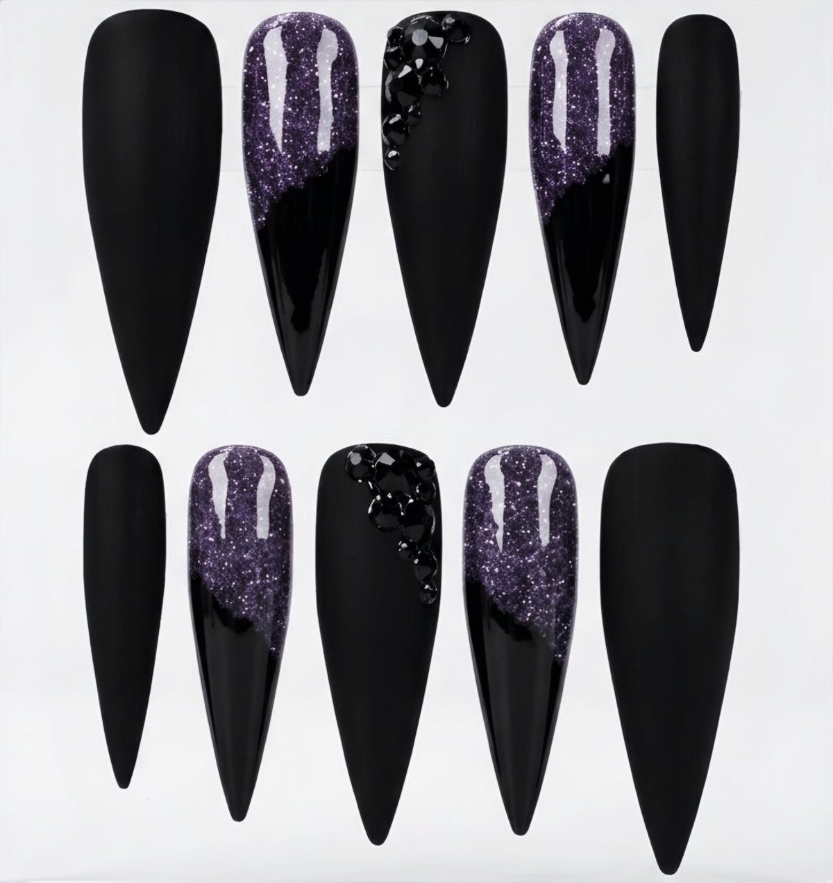 Ten stiletto-shaped press-on nails arranged in two rows on a white background. The nails are primarily black, with three featuring a glittery purple gradient design and one with black rhinestone embellishments.