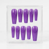 A set of ten purple glitter press-on nails displayed in a clear acrylic box against a white background.