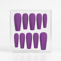 A set of ten matte purple press-on nails in various lengths, displayed inside a clear plastic square box against a white background.