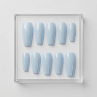 Ten coffin-shaped press-on nails in a glossy light blue shade, arranged in two rows inside a clear square acrylic display box on a white background.