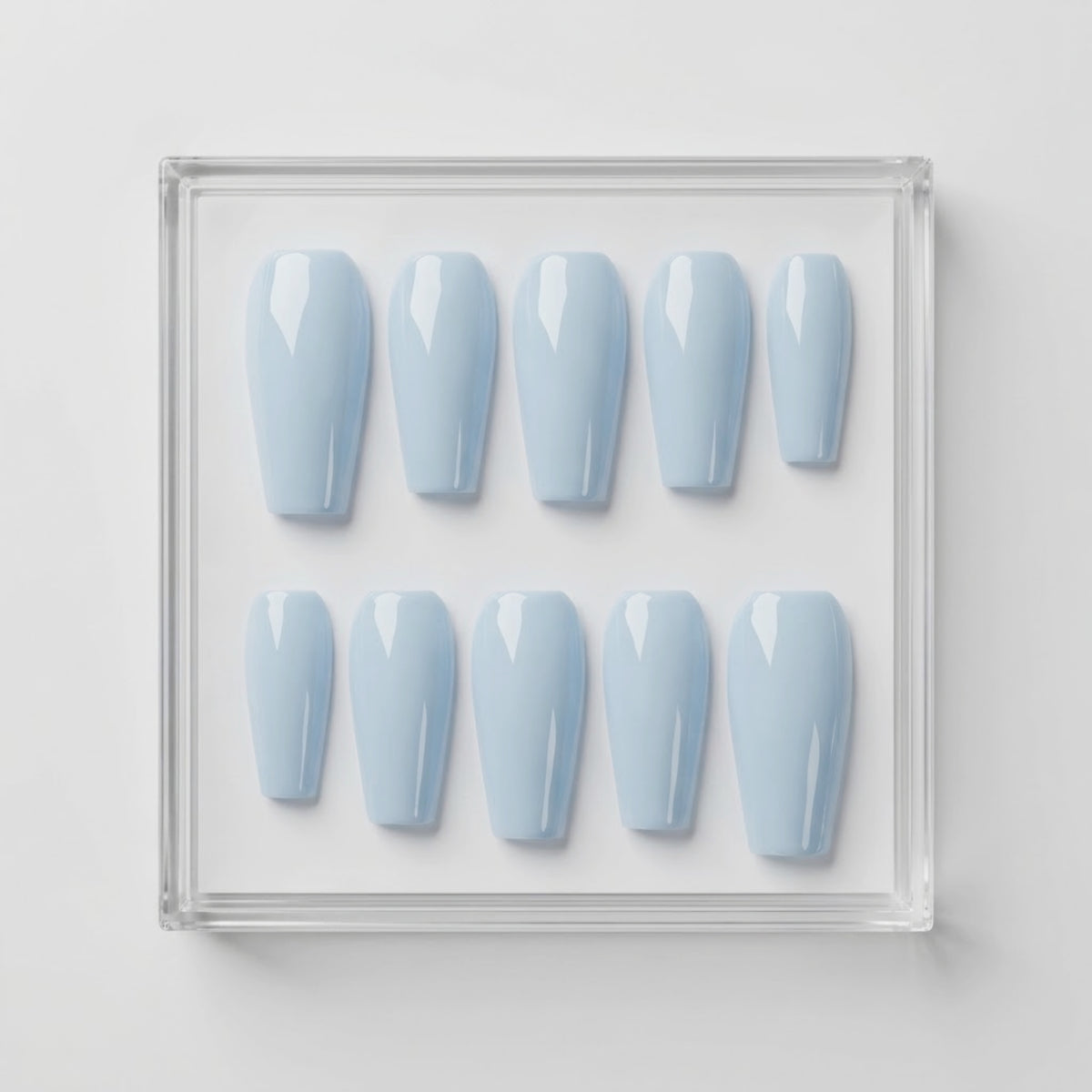 Ten coffin-shaped press-on nails in a glossy light blue shade, arranged in two rows inside a clear square acrylic display box on a white background.