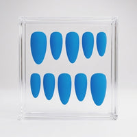 A set of ten bright blue press-on nails arranged in two rows inside a clear acrylic display box on a light gray background.