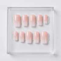 Ten square press-on nails with a soft pink ombre gradient transitioning to white at the tips, displayed in a clear acrylic tray on a white background.