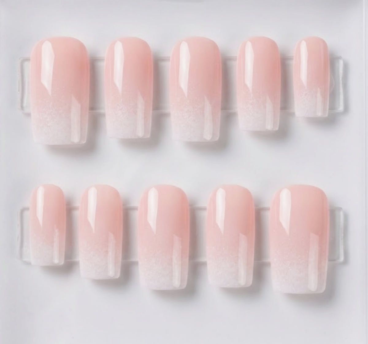 Ten square press-on nails with a glossy pale pink to white ombre gradient, arranged in two rows on a clear display card against a white background.