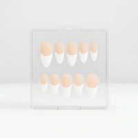 A set of coffin press-on nails in a clear plastic case, featuring a matte french design with white tips and  a light peach nude bases.