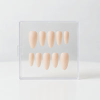 Ten almond beige nude matte press-on nails in a dual-row arrangement inside a clear plastic storage case, set against a seamless white background.
