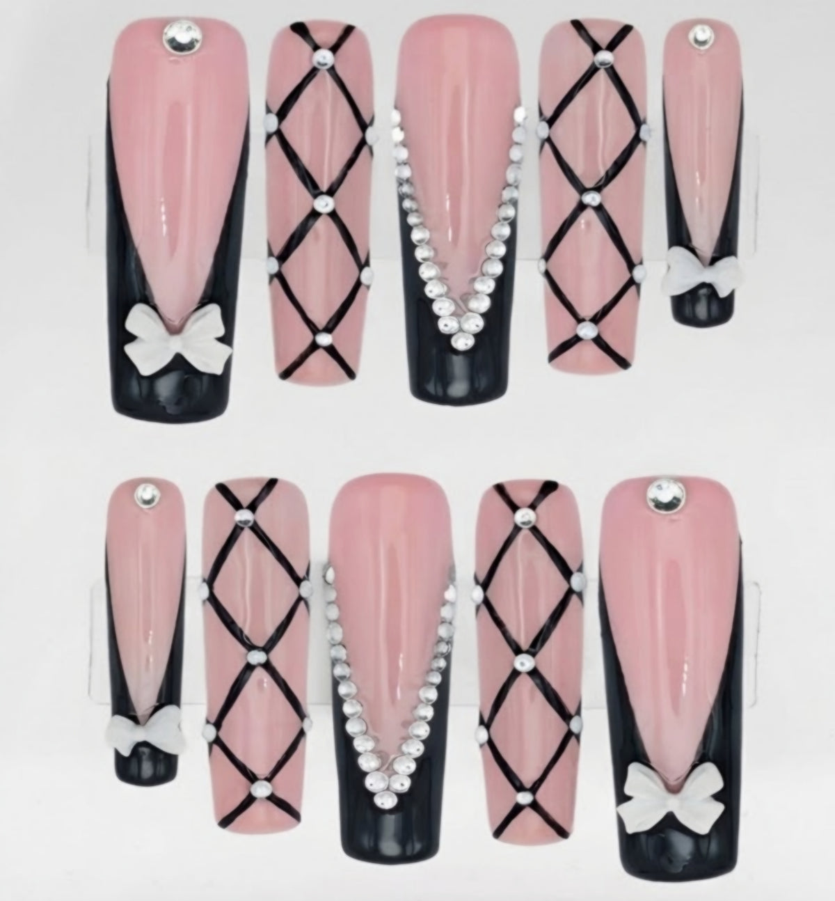 A set of press-on square nails displayed against a white background. The nails feature a glossy pink and black French manicure design with black criss-cross lattice patterns, rhinestones, and white bow accents.