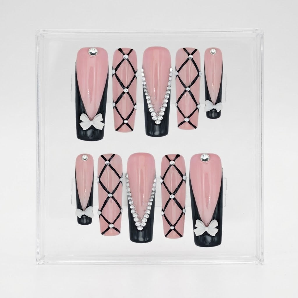 A set of 10 square press-on nails displayed in a clear acrylic case against a white background. The nails feature a pink and black color scheme with various decorative patterns including bows, rhinestones, and geometric diamond grids.