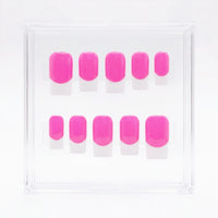 A set of ten bright pink press-on nails with white french tips, arranged in two rows inside a clear square plastic display box on a white background.