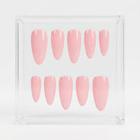 Ten pink press-on nails arranged in two rows inside a clear square acrylic display box on a white background.