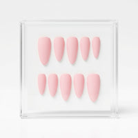 Ten light pink press-on nails arranged in two rows inside a clear acrylic display box on a white background.