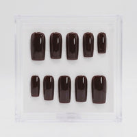 A set of glossy dark brown press-on nails arranged in two rows inside a clear square display box on a white background.