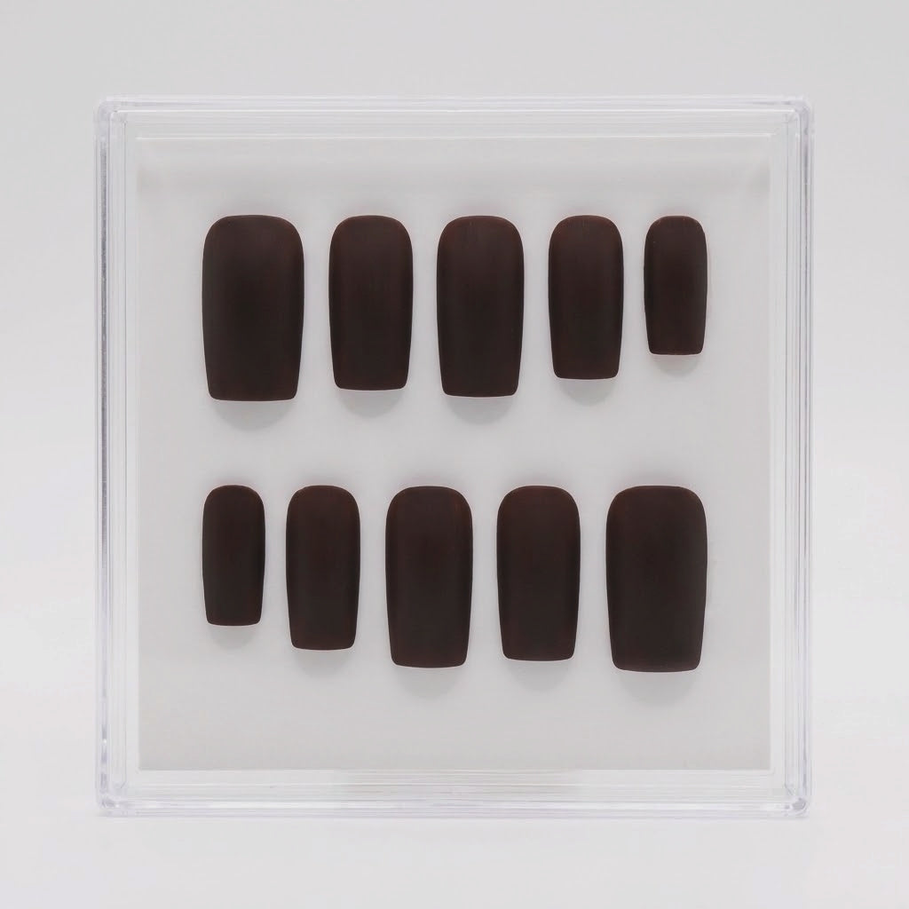 A set of ten dark brown press-on nails arranged in two rows inside a clear plastic display box on a light gray background.