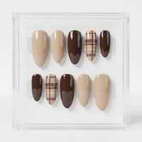 A set of 10 press-on nails displayed in a clear acrylic case against a white background. The nails feature various designs including solid dark brown, solid beige, and beige and brown plaid patterns.