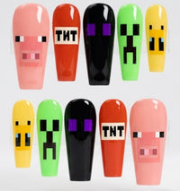 Ten glossy coffin-shaped press-on nails featuring Minecraft-inspired designs, including a pig face, TNT explosion, black zombie eyes, green creeper face, and yellow block character faces, arranged in two rows on a white background.