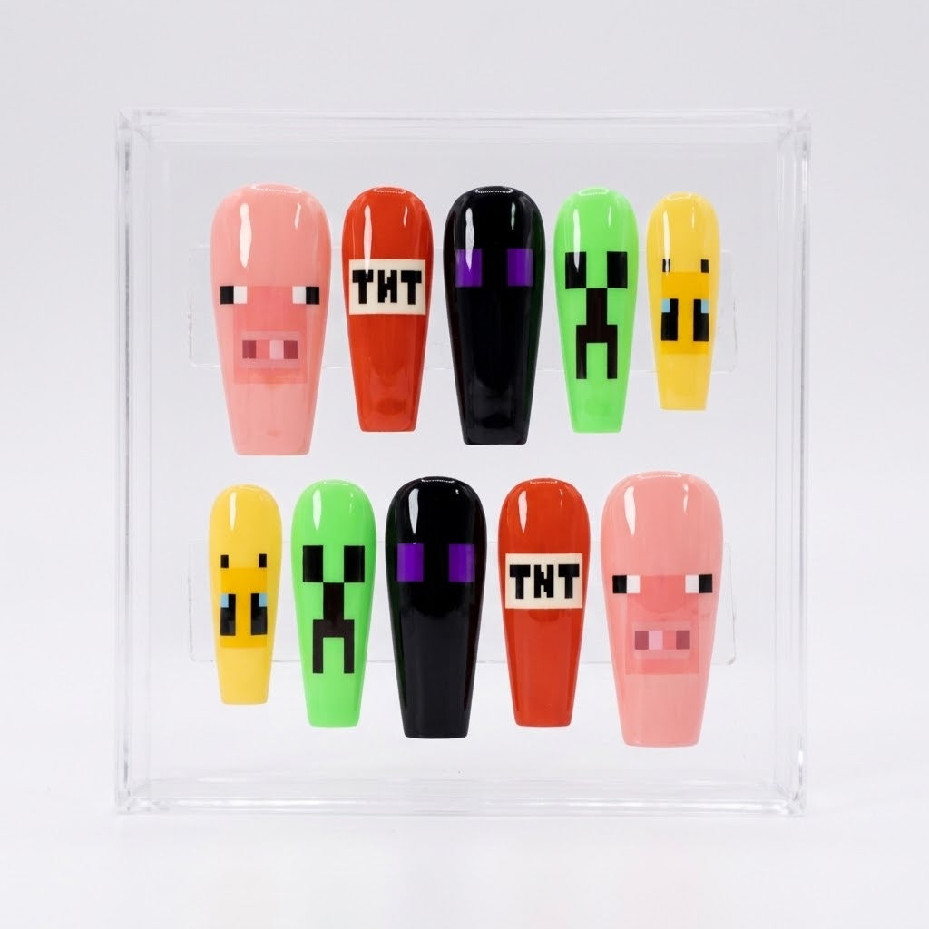 A set of 10 glossy coffin-shaped press-on nails displayed in a clear acrylic case. The nails feature pixelated Minecraft-style designs, including pink pigs, green creepers, yellow slimes, and red TNT boxes.