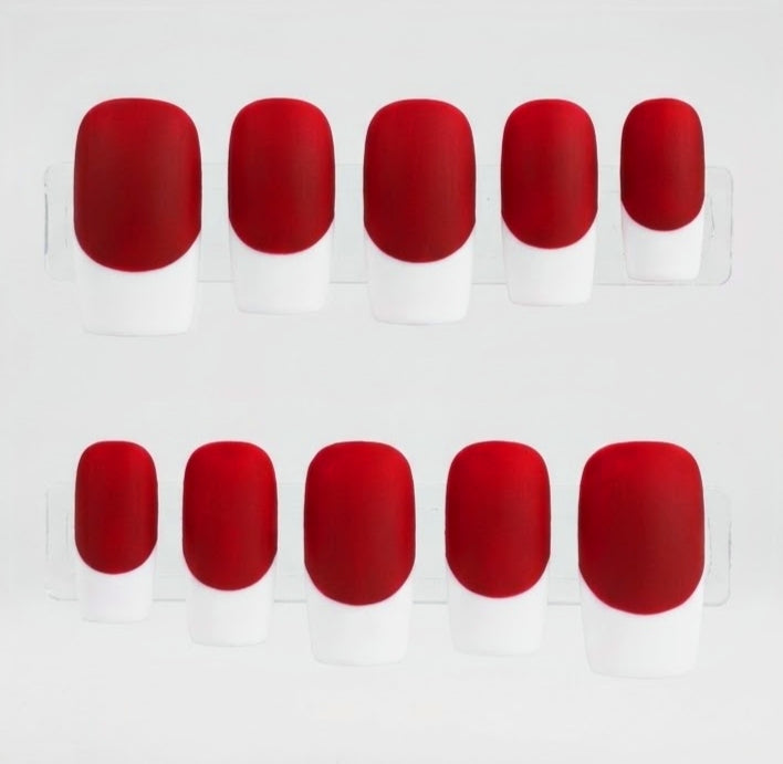 Ten false press-on nails arranged in two rows of five on a clear display stand, featuring a bright matte red base and a white french tip, set against a plain white background.