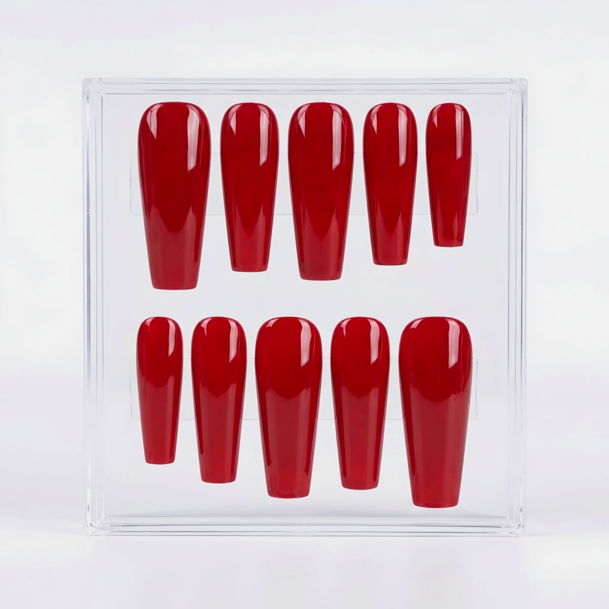 Ten coffin shaped bright red press on nails in a glossy finish, in a clear case on a white backgroung.
