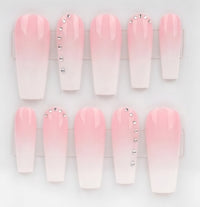 A set of coffin-shaped press-on nails with a pink-to-white ombre gradient, decorated with silver rhinestones on two of the nails, displayed in a clear plastic case against a white background.