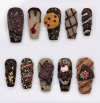 Ten decorative false nails arranged in two rows on a white background, featuring chocolate-themed designs including chocolate bars, drizzles, cookie details, whipped cream, and sweet treats.