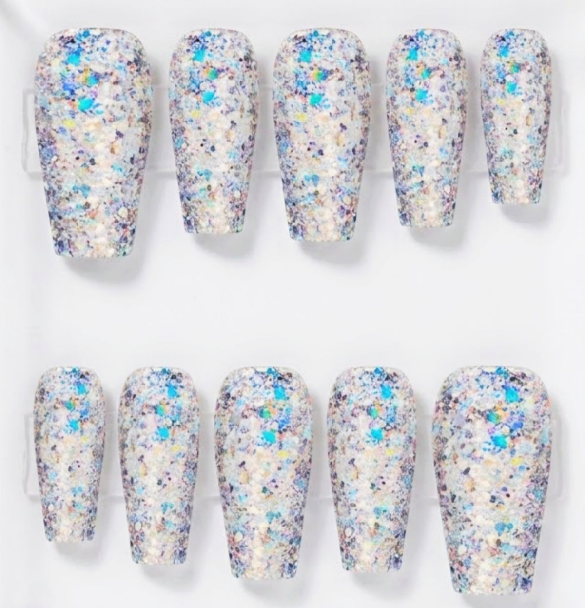 Ten false press-on nails arranged in two rows of five on a clear display stand, featuring a dense glitter finish with iridescent blue, purple, and gold flakes over a white base.