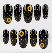 Ten glossy oval black press-on nails with yellow polka dots and two yellow sunflower designs, displayed  against a white background.