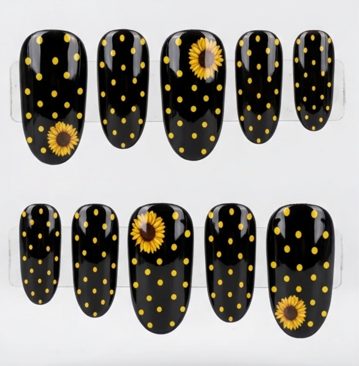 Ten glossy oval black press-on nails with yellow polka dots and two yellow sunflower designs, displayed  against a white background.