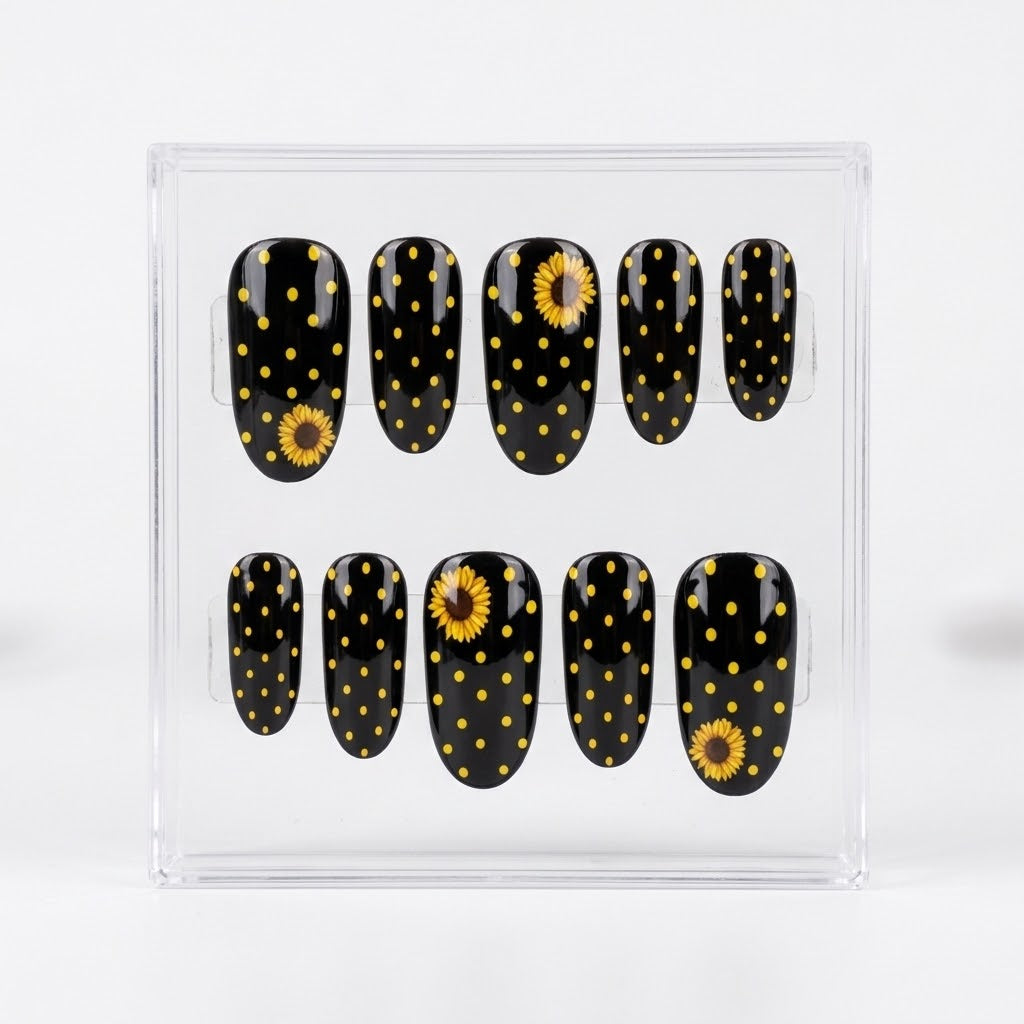 A set of ten glossy oval press-on nails displayed in a clear plastic case, featuring a black background with yellow polka dots and sunflower designs.