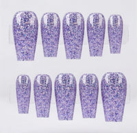 Ten press-on nails with a glittery lavender purple finish, arranged in two rows of five on a clear display stand against a white background.