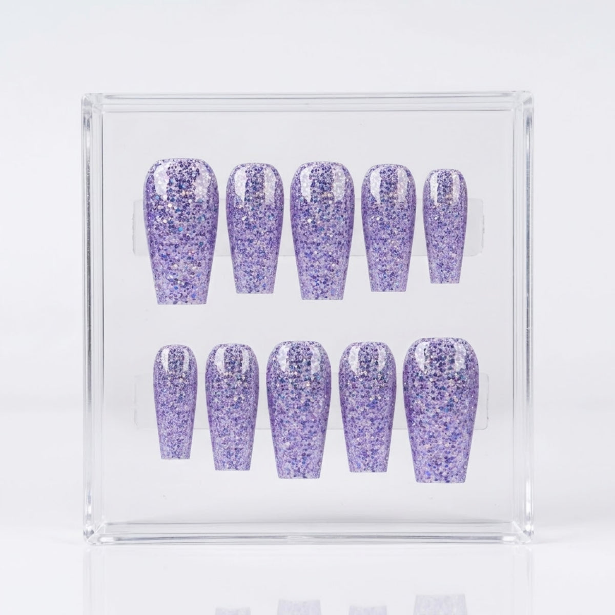 A set of ten glittery lavender-purple press-on nails displayed inside a clear acrylic box against a white background.