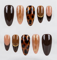 Ten press-on nails displayed on clear plastic stands against a light gray background. The set includes glossy dark brown, nude beige, tortoiseshell brown, and dark brown with gold accent lines.