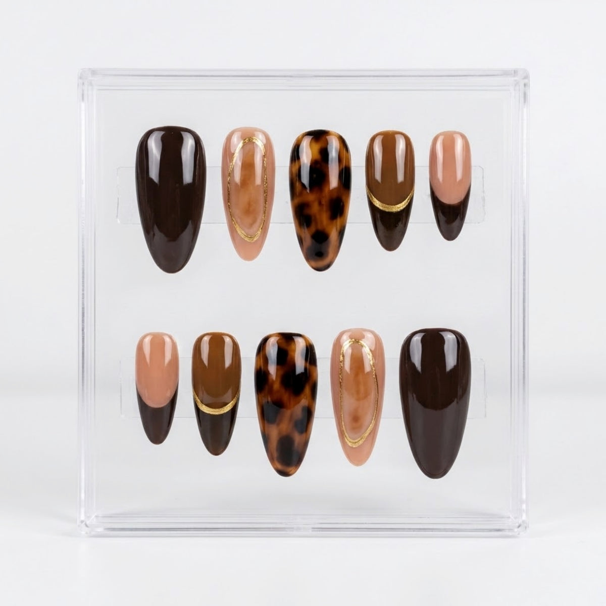 A set of ten press-on nails displayed in a clear acrylic case against a white background. The nails feature various designs in shades of brown, beige, and black, including solid dark brown, nude beige, leopard print, and marbled patterns with thin gold accent lines.