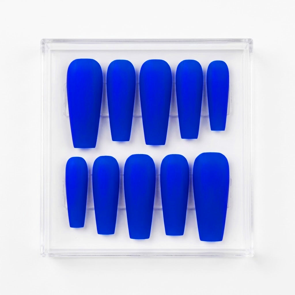 A set of ten long coffin-shaped press-on nails in a neon royal blue color, neatly arranged inside a clear plastic display box on a white background.