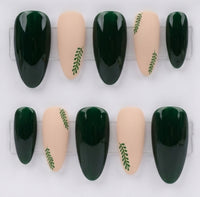 Ten press-on nails arranged in two rows on a clear display stand against a white background. The nails feature a glossy deep green and a matte nude beige, with some nude nails decorated with a small green leaf motif.