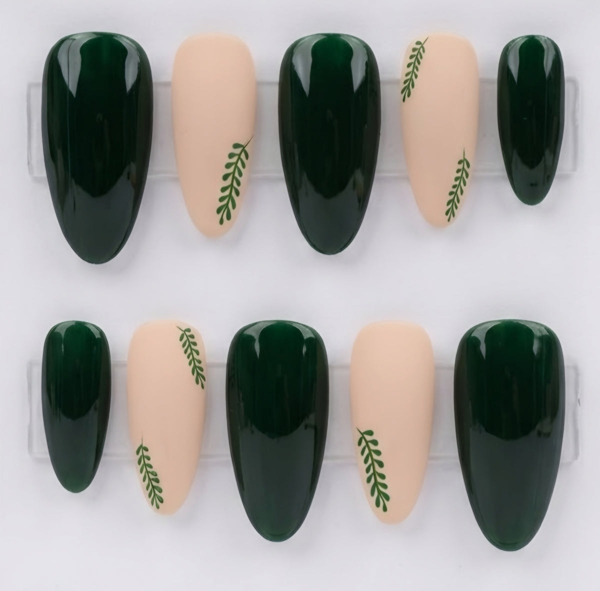 Ten press-on nails arranged in two rows on a clear display stand against a white background. The nails feature a glossy deep green and a matte nude beige, with some nude nails decorated with a small green leaf motif.