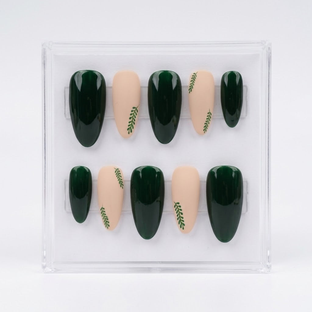 A set of 10 press-on false nails in an oval shape, displayed inside a clear plastic case. The nails feature a color-blocked design with dark forest green and nude beige, accented with small green leaf patterns on the nude nails.
