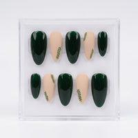 A set of 10 press-on false nails in an oval shape, displayed inside a clear plastic case. The nails feature a color-blocked design with dark forest green and nude beige, accented with small green leaf patterns on the nude nails.