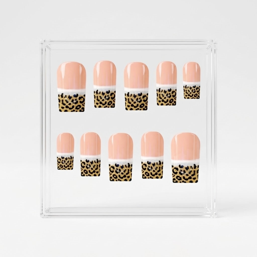 A set of ten square false press-on nails displayed inside a clear acrylic square box on a light gray background. The nails feature a glossy peach-pink top half, a white middle band, and a leopard print bottom half with black spots on a gold background.