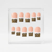A set of ten square false press-on nails displayed inside a clear acrylic square box on a light gray background. The nails feature a glossy peach-pink top half, a white middle band, and a leopard print bottom half with black spots on a gold background.