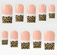 Ten square press on nails arranged in two rows on a plain white background. Each nail has a glossy peach-pink top section, a thin white band, and a leopard-print lower section with black spots on a gold background.