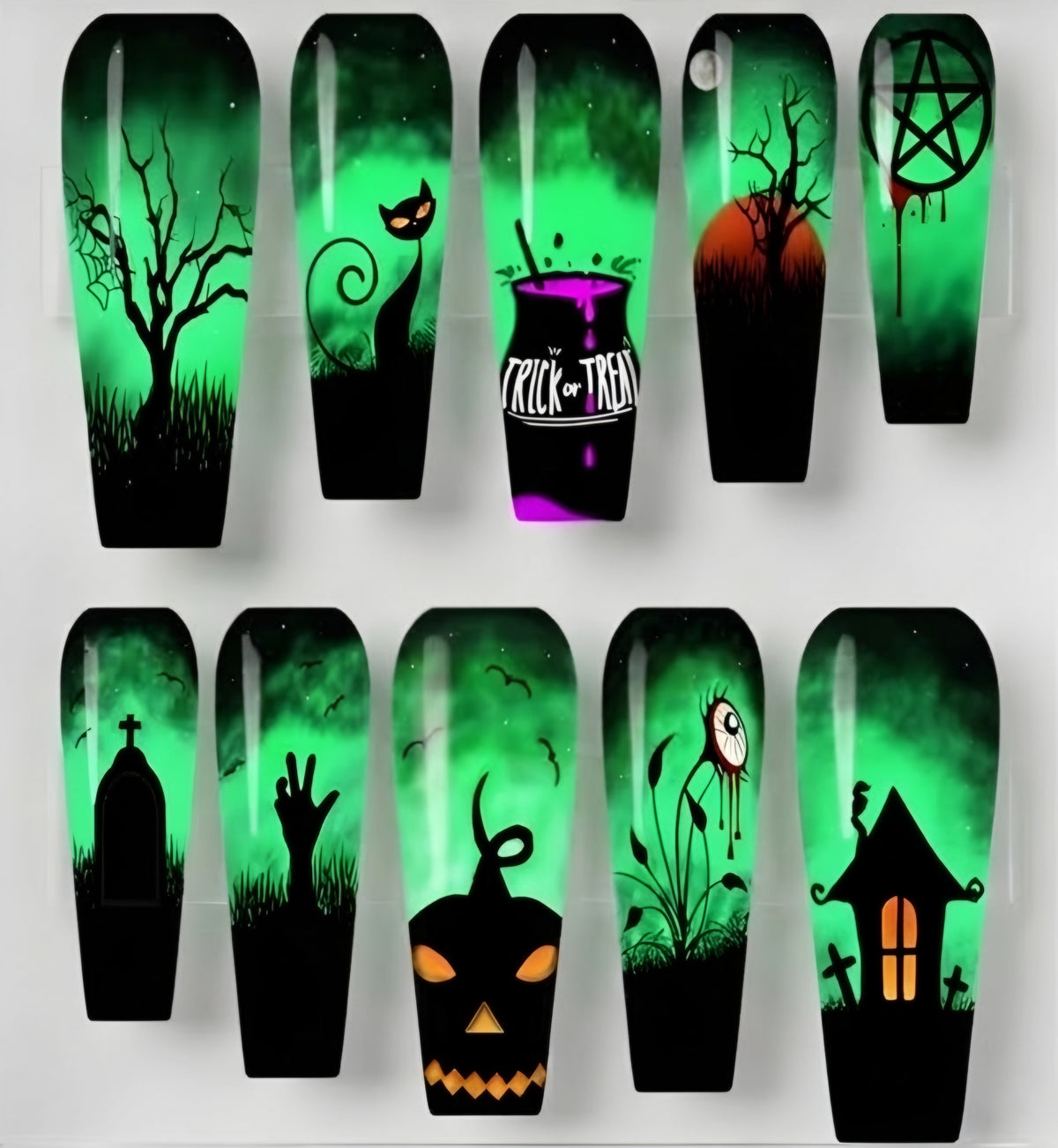 Ten coffin-shaped press on nails arranged in two rows on a light gray background, each featuring a different spooky Halloween design like a bare tree, cat, potion bottle, pentagram, tombstone, zombie hand, jack-o'-lantern, spider, and haunted house, all in black and green with small orange accents.