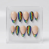 A set of 10 almond press-on nails displayed in a clear acrylic case. The nails feature a split design with a smooth nude-beige half and a black wing-patterned half decorated with a vibrant rainbow gradient.