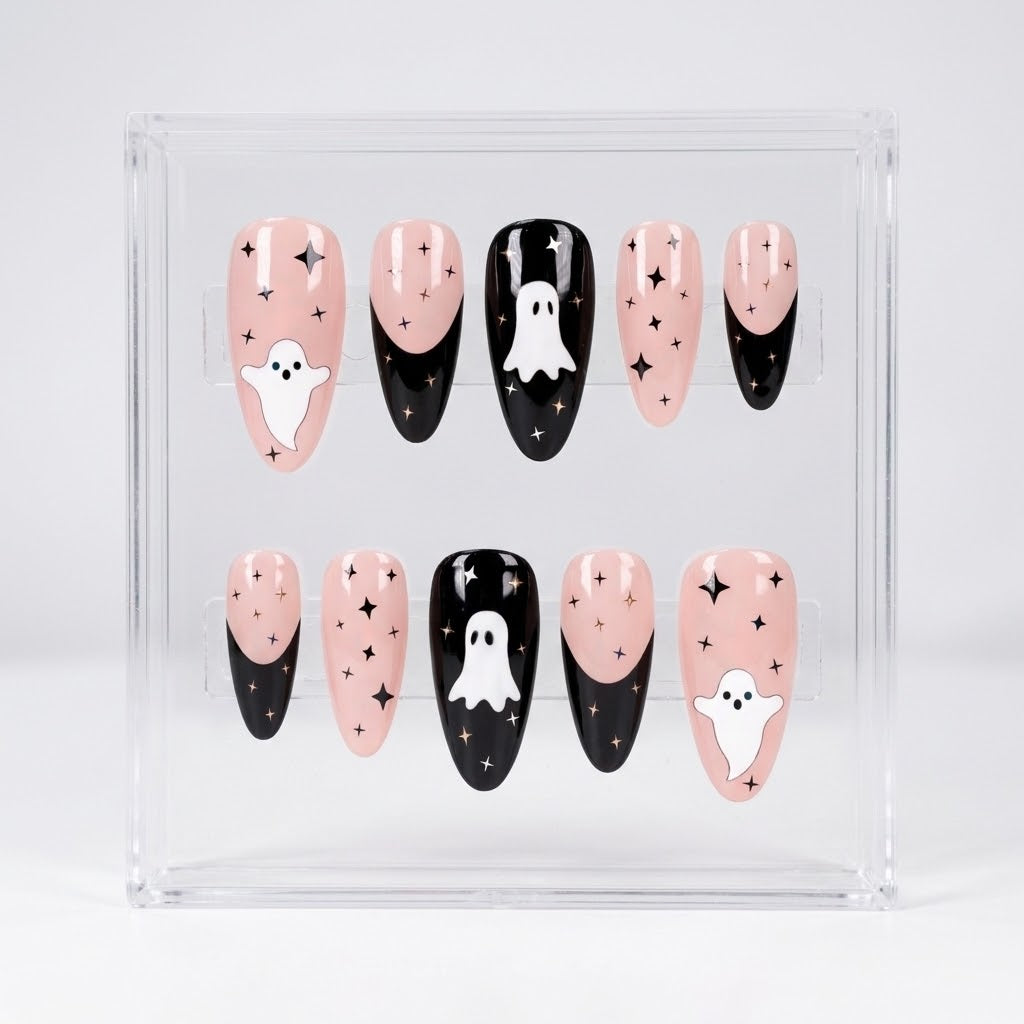 A set of Halloween-themed glossy press-on nails displayed in a clear acrylic case. The nails feature a pink-to-black French tip design with white ghost illustrations and small gold star accents.