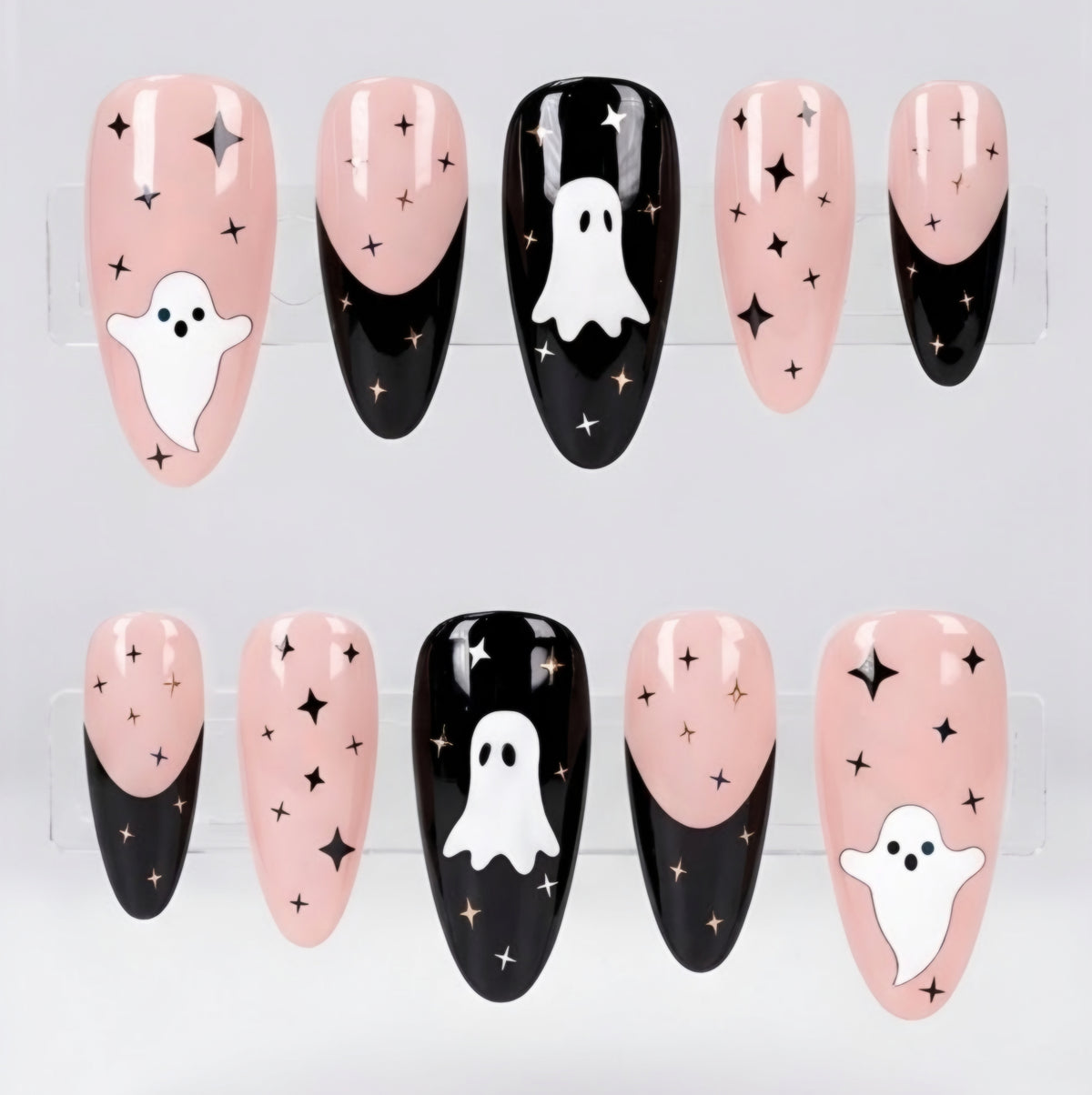 Set of glossy 10 press-on nails with a pink and black French tip design, decorated with white ghosts and black stars, displayed on clear stands against a white background.