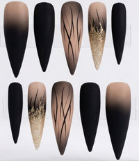 Ten stiletto-shaped press-on nails arranged in two rows on a white display card. The nails feature black ombre gradients, solid black tips, nude beige-to-black gradients with thin black line patterns, and glittery gold sparkles.