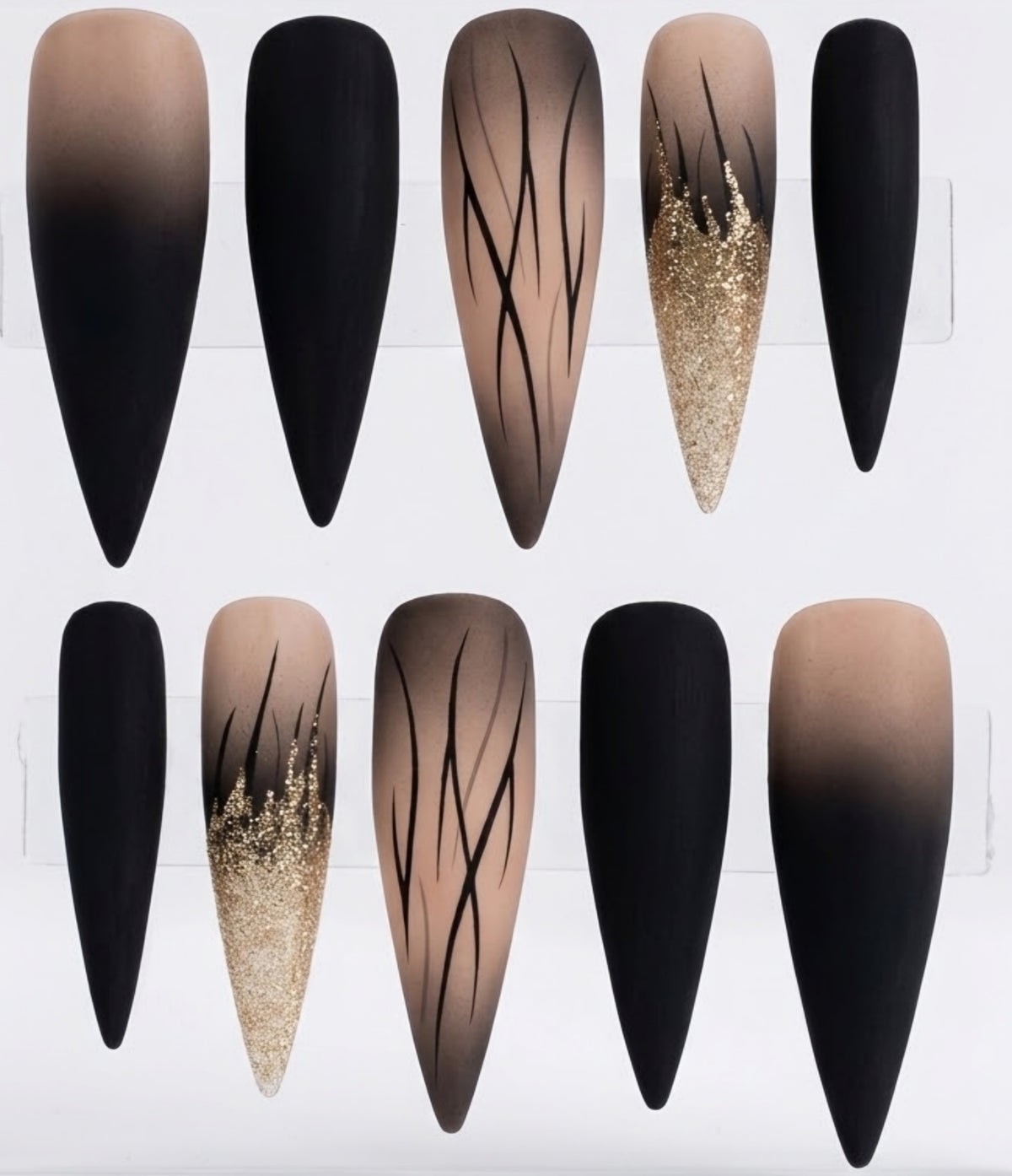 Ten stiletto-shaped press-on nails arranged in two rows on a white display card. The nails feature black ombre gradients, solid black tips, nude beige-to-black gradients with thin black line patterns, and glittery gold sparkles.
