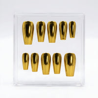 Ten metallic gold chrome coffin-shaped press-on nails arranged inside a clear plastic display box on a white background.