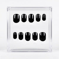 Ten black press-on nails with white french tips, arranged in two rows inside a clear acrylic display box on a white background.