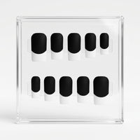Ten matte black press-on nails with white french tips, arranged in two rows inside a clear acrylic display box on a white background.